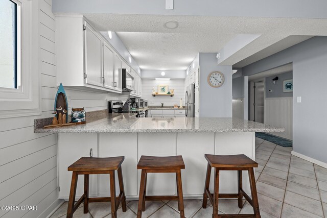5801 Thomas Dr Unit 601, Panama City Beach, FL 32408 - kitchen with white cabinets, stainless steel appliances, a peninsula, a textured ceiling, and a breakfast bar area