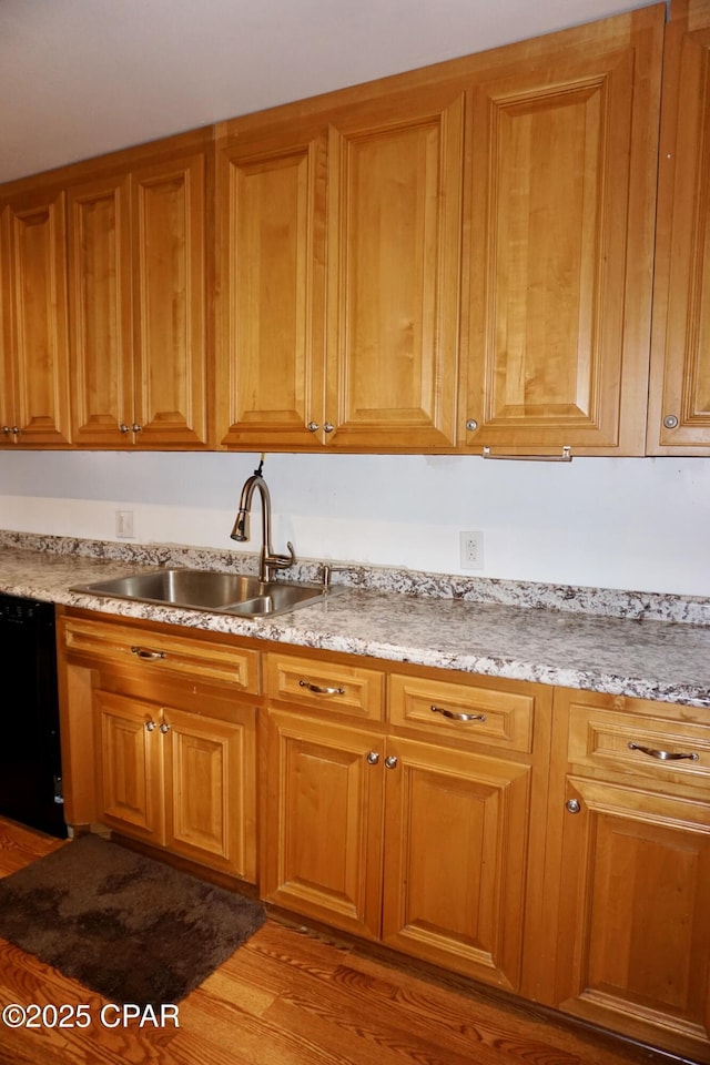 kitchen with wood finished floors, a sink, light stone countertops, dishwasher, and brown cabinetry