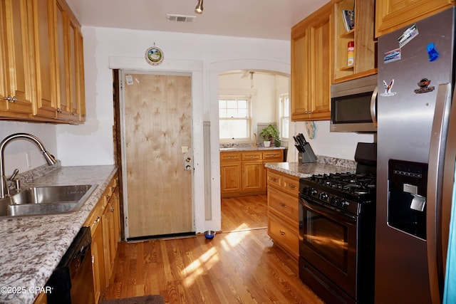 kitchen with visible vents, arched walkways, light wood-style flooring, black appliances, and a sink