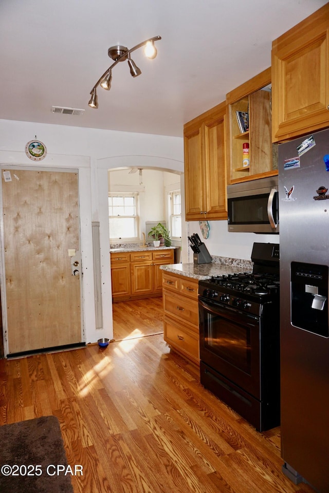 kitchen with visible vents, arched walkways, light wood-style flooring, light stone countertops, and stainless steel appliances