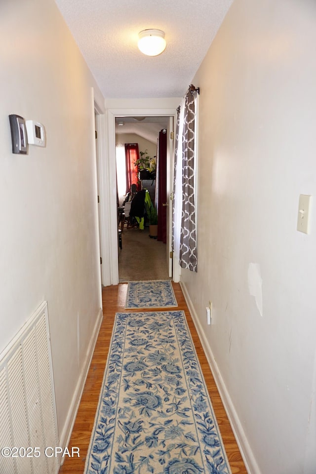 hallway with visible vents, a textured ceiling, baseboards, and wood finished floors