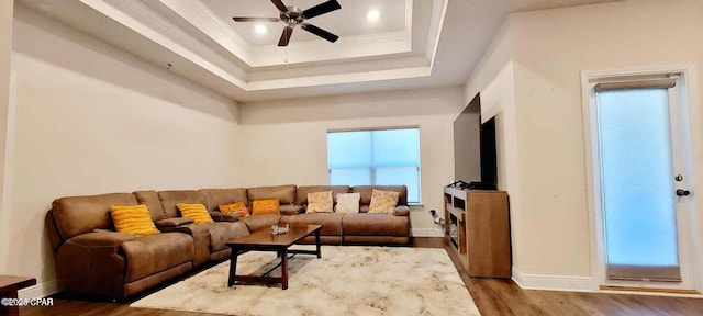 living room with a raised ceiling, ornamental molding, hardwood / wood-style floors, and ceiling fan