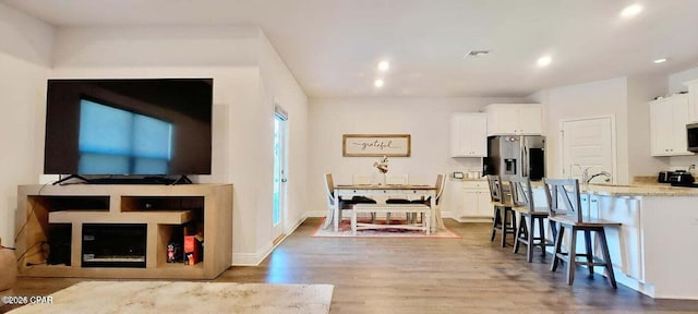 kitchen with light hardwood / wood-style flooring, a kitchen breakfast bar, stainless steel appliances, light stone countertops, and white cabinets