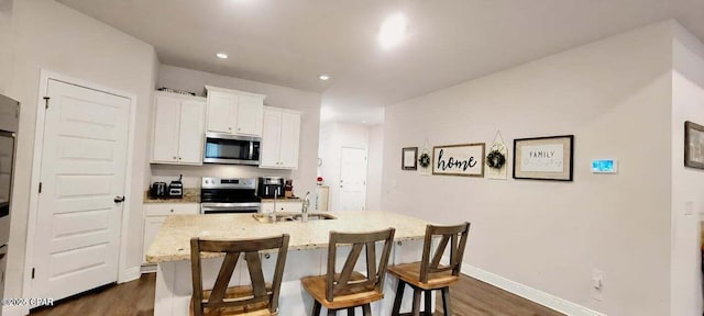 kitchen featuring a kitchen breakfast bar, stainless steel appliances, light stone countertops, a kitchen island with sink, and white cabinets