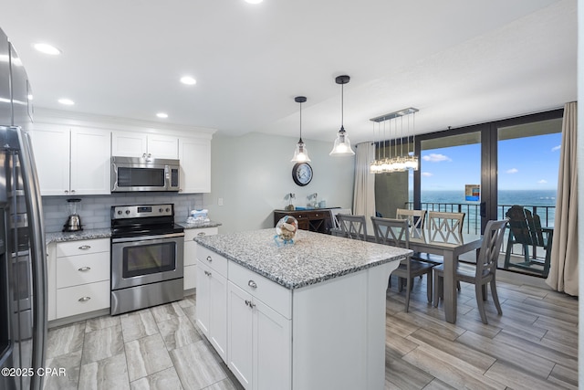 kitchen with tasteful backsplash, appliances with stainless steel finishes, white cabinetry, light stone countertops, and a kitchen island