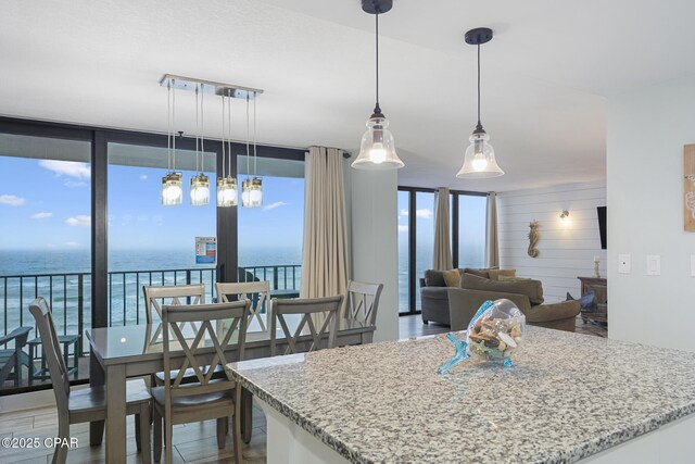 kitchen featuring floor to ceiling windows, a water view, light stone counters, pendant lighting, and hardwood / wood-style floors