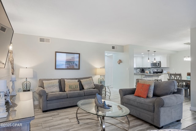 living area featuring light wood-style floors, a notable chandelier, and visible vents