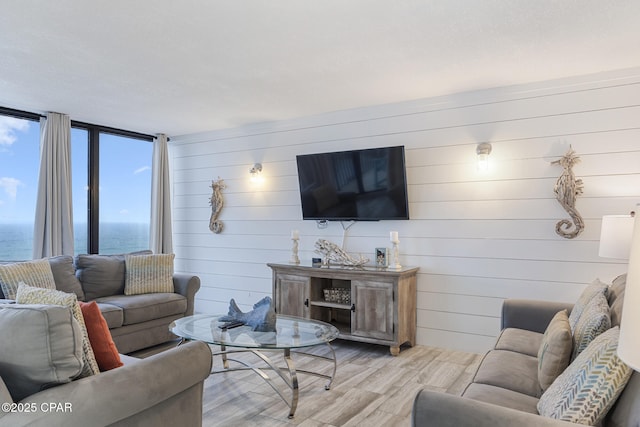 living area featuring light wood-style floors, wooden walls, plenty of natural light, and a water view