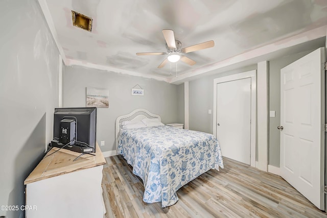 bedroom featuring ceiling fan, a raised ceiling, a closet, and light hardwood / wood-style flooring