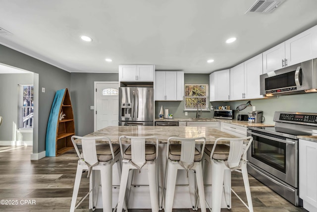 kitchen featuring light stone counters, stainless steel appliances, a center island, and white cabinets