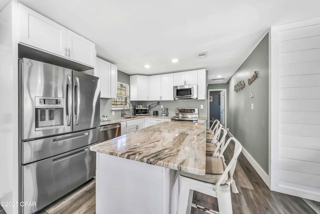 kitchen with light stone countertops, appliances with stainless steel finishes, white cabinets, and a kitchen breakfast bar