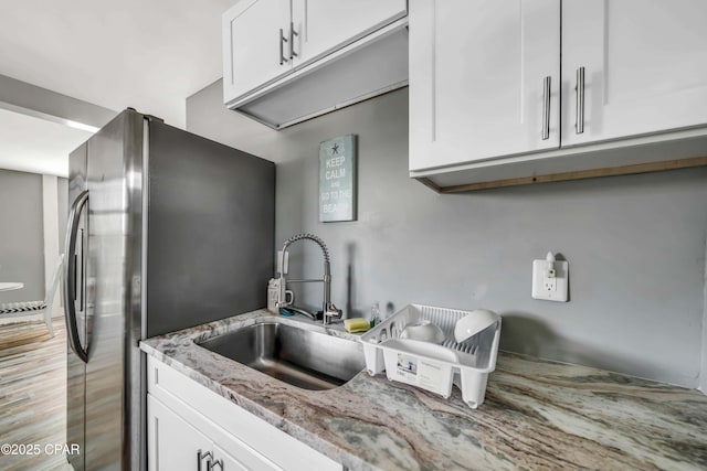 kitchen with stainless steel refrigerator with ice dispenser, light stone countertops, sink, and white cabinets