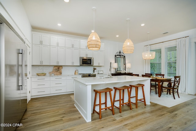 kitchen with a kitchen breakfast bar, backsplash, light wood-style floors, appliances with stainless steel finishes, and white cabinets