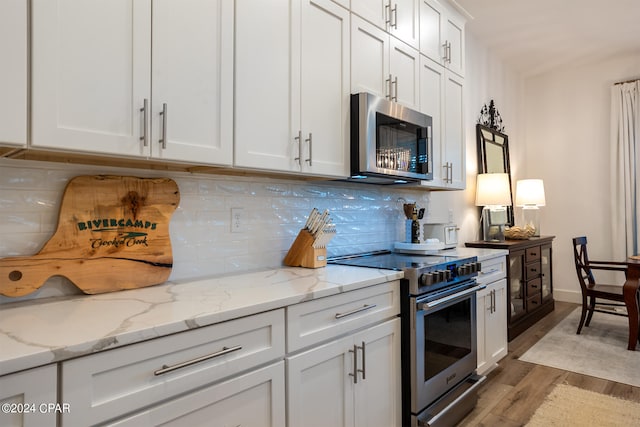 kitchen with light stone counters, backsplash, white cabinetry, stainless steel appliances, and light wood-style floors