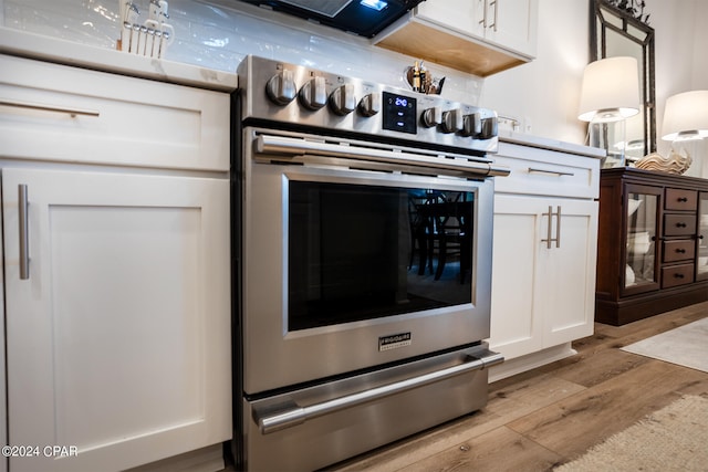 kitchen with stainless steel range with electric stovetop, white cabinets, light countertops, and light wood finished floors