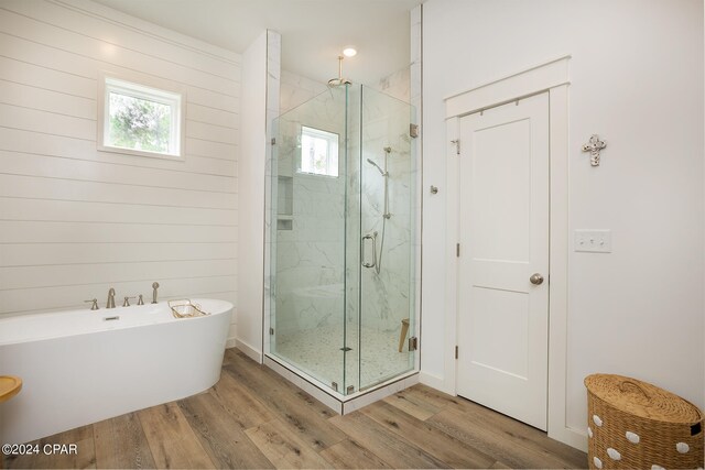 full bath featuring a wealth of natural light, a marble finish shower, a soaking tub, and wood finished floors