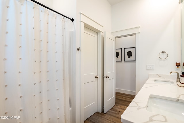 bathroom with a sink, a shower with shower curtain, wood finished floors, and double vanity