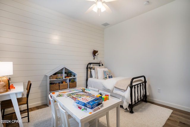 bedroom with visible vents, a ceiling fan, wood finished floors, wooden walls, and baseboards