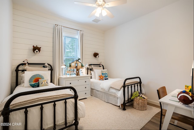 bedroom with a ceiling fan, wooden walls, wood finished floors, and baseboards