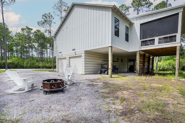 back of house with driveway, a fire pit, an attached garage, a sunroom, and a carport