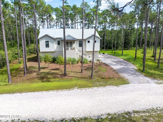 view of front facade featuring metal roof, a front yard, board and batten siding, and driveway