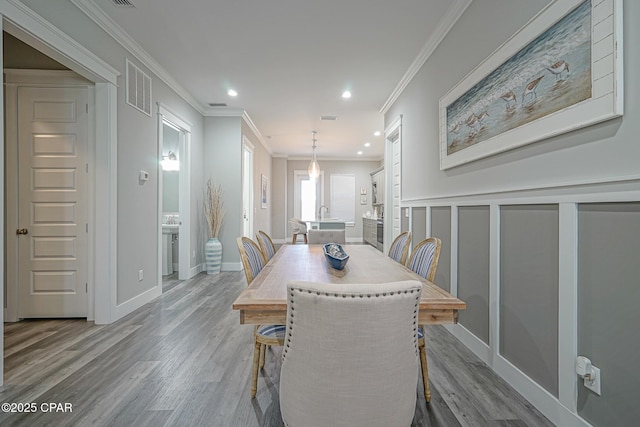 dining room with crown molding, recessed lighting, visible vents, a decorative wall, and wood finished floors