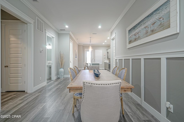 dining space featuring visible vents, wood finished floors, crown molding, a decorative wall, and recessed lighting