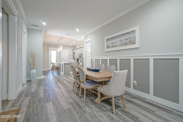 dining area featuring a decorative wall, recessed lighting, visible vents, light wood-style floors, and crown molding