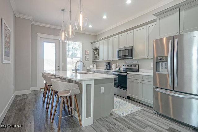 kitchen featuring appliances with stainless steel finishes, a breakfast bar, ornamental molding, a kitchen island with sink, and a sink