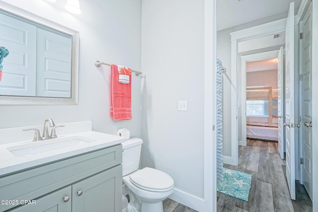 ensuite bathroom with ensuite bathroom, toilet, wood finished floors, vanity, and baseboards