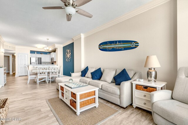 living room with crown molding, ceiling fan with notable chandelier, and light hardwood / wood-style floors