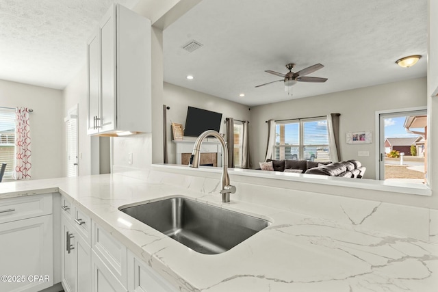 kitchen featuring light stone counters, sink, kitchen peninsula, and white cabinets