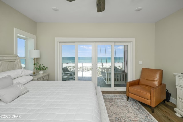 bedroom with hardwood / wood-style floors, access to outside, ceiling fan, a water view, and a beach view