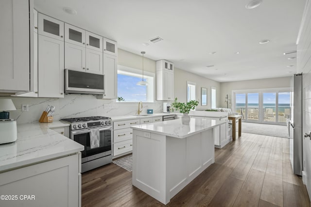 kitchen with gas range, decorative light fixtures, a center island, light stone countertops, and white cabinets