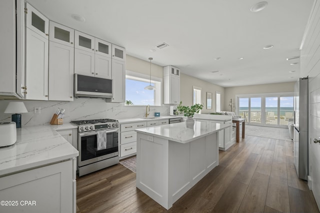 kitchen featuring a kitchen island, white cabinetry, hanging light fixtures, light stone countertops, and stainless steel range with gas stovetop