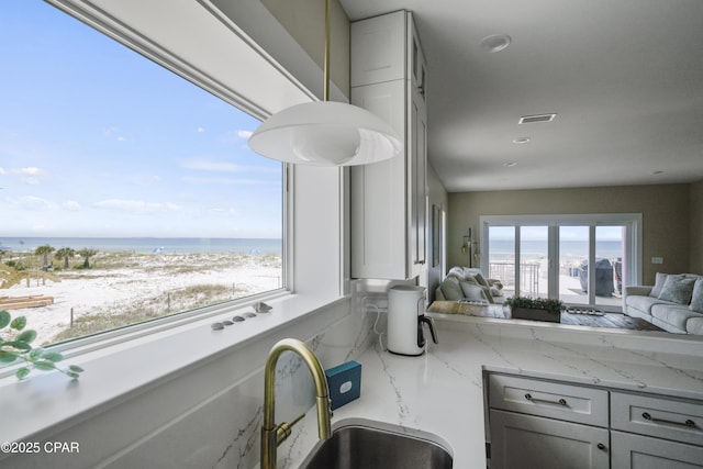 interior space featuring a water view, plenty of natural light, a view of the beach, and light stone counters