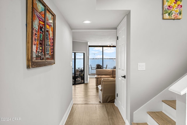 hall featuring light wood-type flooring, floor to ceiling windows, and a water view