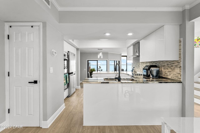 kitchen featuring sink, crown molding, light wood-type flooring, kitchen peninsula, and white cabinets