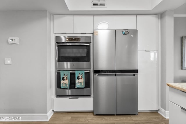 kitchen with stainless steel appliances, white cabinetry, and light hardwood / wood-style flooring