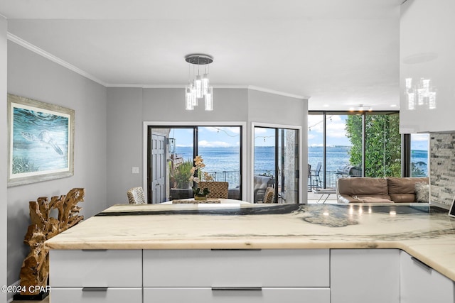 kitchen with crown molding, white cabinetry, hanging light fixtures, a water view, and a chandelier