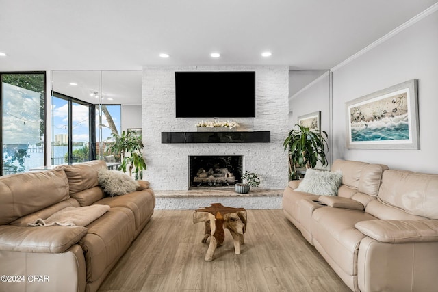 living room with crown molding, a stone fireplace, and light hardwood / wood-style flooring