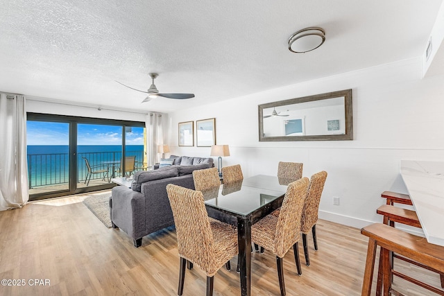 dining space featuring a water view, ceiling fan, light hardwood / wood-style floors, and a textured ceiling