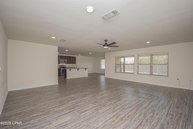 unfurnished living room featuring ceiling fan, plenty of natural light, dark hardwood / wood-style floors, and a textured ceiling