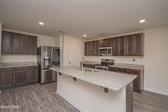 kitchen with dark brown cabinetry, sink, stainless steel appliances, and an island with sink