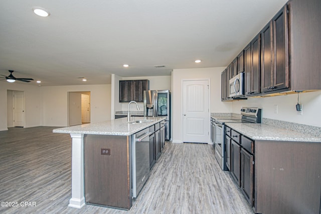 kitchen with sink, light hardwood / wood-style flooring, appliances with stainless steel finishes, dark brown cabinets, and an island with sink