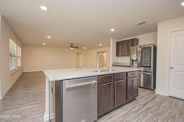 kitchen with sink, appliances with stainless steel finishes, dark brown cabinets, a center island with sink, and light wood-type flooring