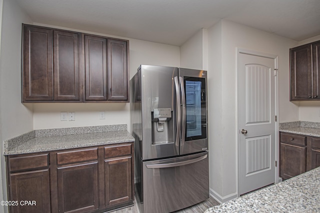 kitchen featuring dark brown cabinetry, stainless steel fridge, and light stone countertops