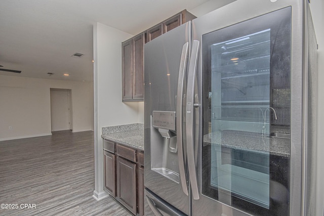 kitchen featuring stone counters, stainless steel fridge, dark brown cabinets, and light wood-type flooring