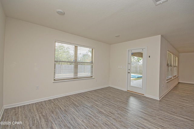 unfurnished room with a healthy amount of sunlight, a textured ceiling, and light hardwood / wood-style flooring