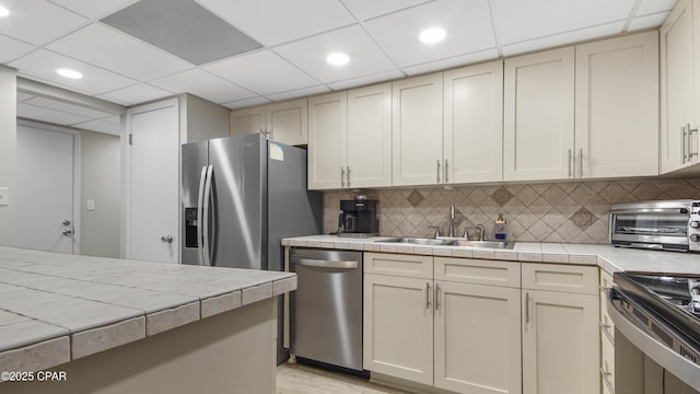 kitchen with sink, appliances with stainless steel finishes, backsplash, tile countertops, and cream cabinetry